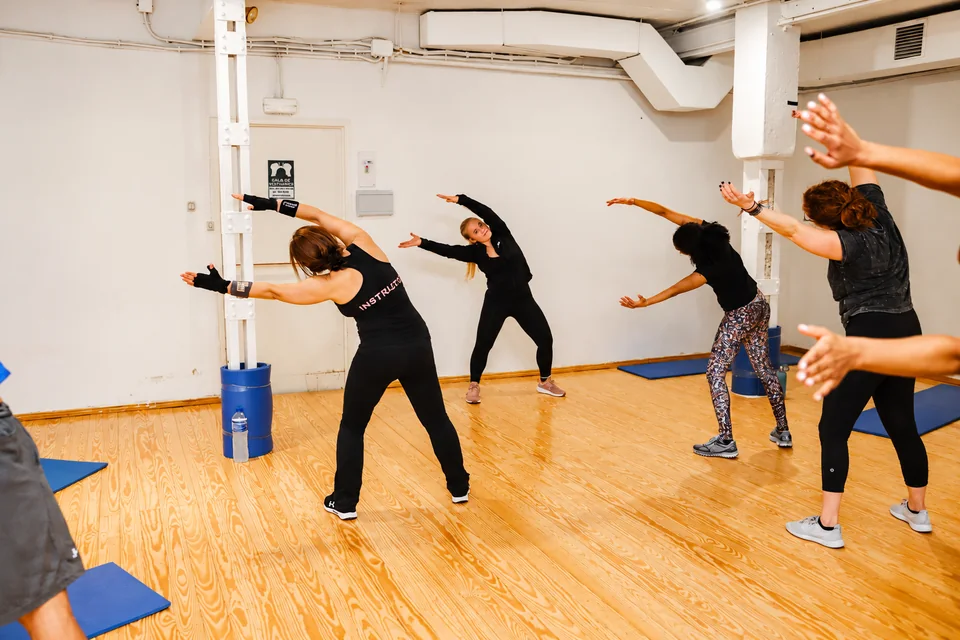 AI-enhanced recreation of a Move With Intention session: a group moves through a side stretch together in a bright studio.