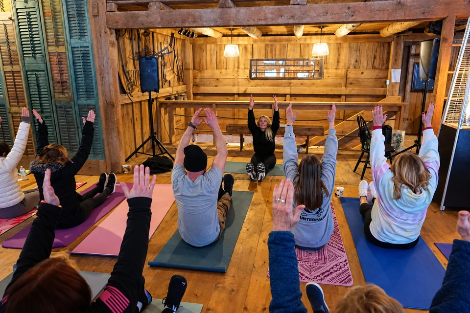 AI-enhanced recreation of a Move With Intention session: participants seated on mats reach their arms overhead at their own pace in a wooden barn studio.